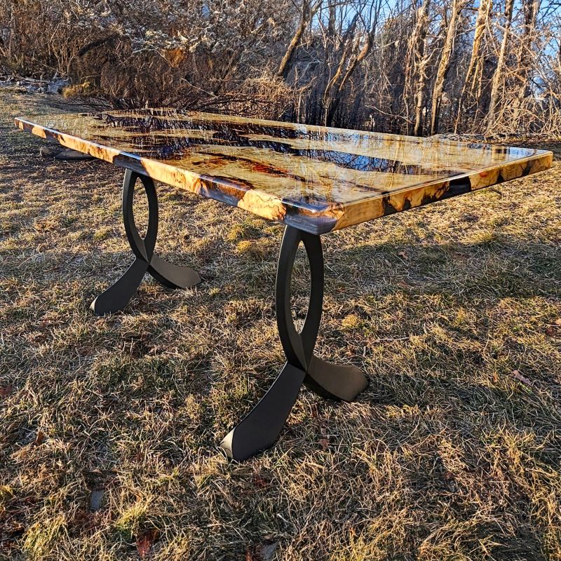 Wood slab table with curved design metal legs for table in natural outdoor setting.