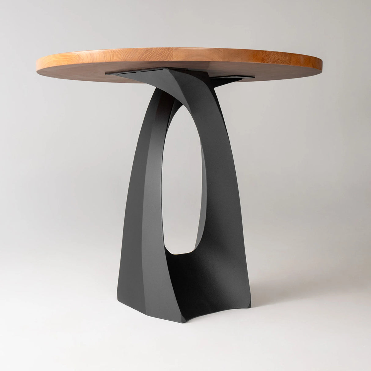 Side view of round wood top table supported by a 610B Tulipe 34" H metal base for counter table in a curved cross shape.