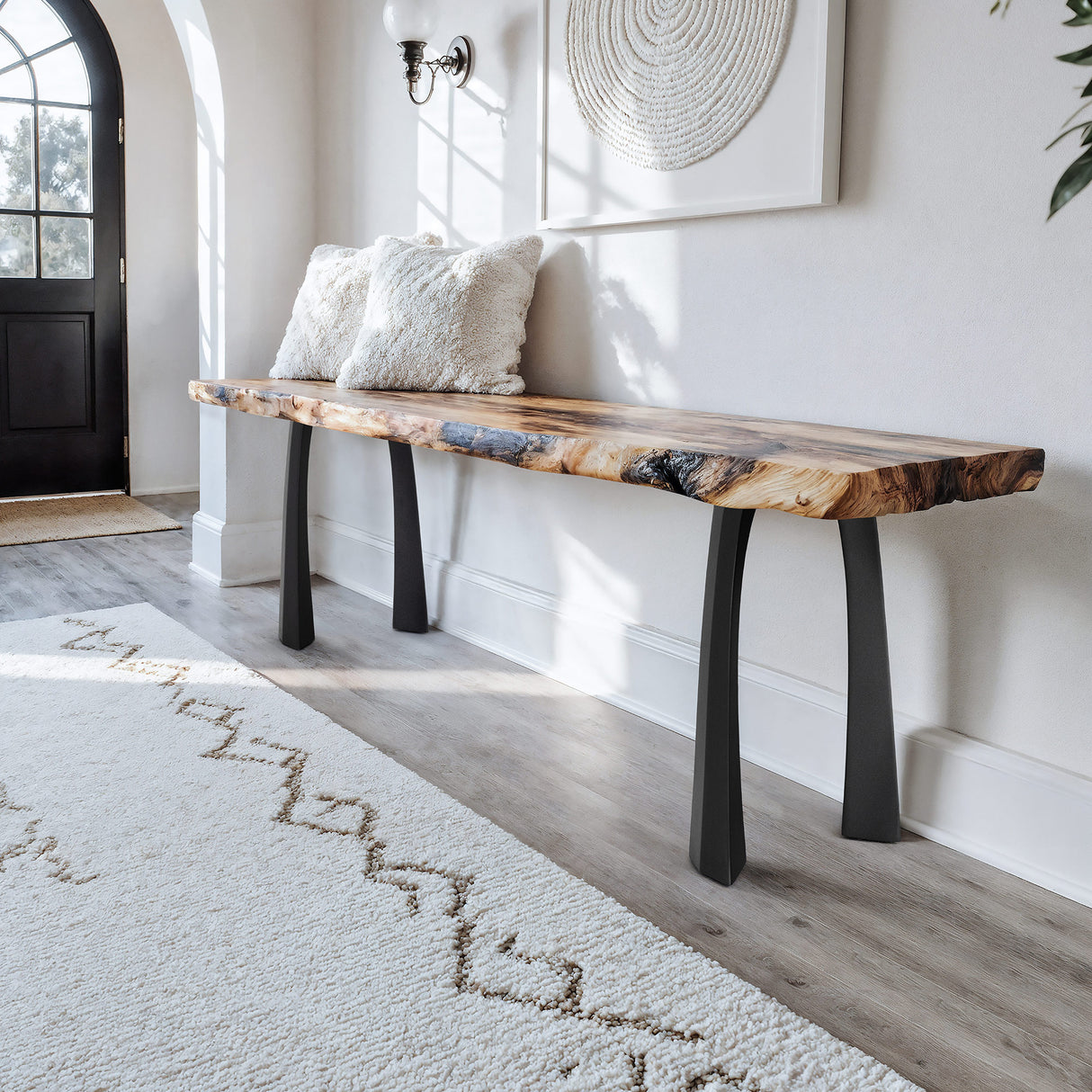 wooden bench with black legs in a room with a rug and wall art