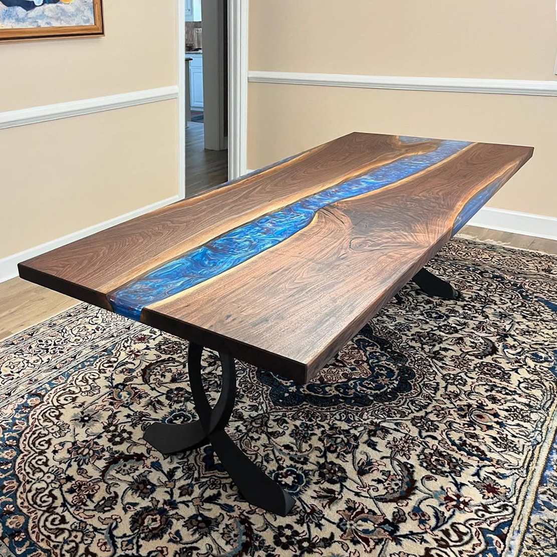 Epoxy river table on curved design metal table legs in indoor setting.