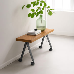 wooden table with wheels, green vase, and books against a white wall