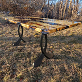Wood slab table with curved design metal legs for table in natural outdoor setting.
